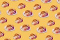 Creative pattern made of freshly baked croissant with flowers on pastel yellow background