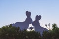 Creative photo of two silhouette paper rabbits in the chamomile flowers and green grass on the sunset sky background Royalty Free Stock Photo