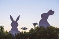 Creative photo of two silhouette paper rabbits in the chamomile flowers and green grass on the sunset sky background Royalty Free Stock Photo