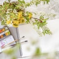 Creative place of the artist, open sketchbook for ideas, watercolor paints, brushes and flowers for inspiration, leisure