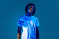 Creative portrait of african young man with dread with neon light reflection on body standing against blue background in