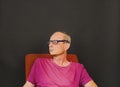 Creative portrait. Middle aged man with glasses sitting in an armchair. Portrait of mature man on black background Royalty Free Stock Photo