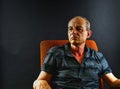 Creative portrait. Middle aged man sitting in an armchair. Portrait of mature man on black background. Royalty Free Stock Photo