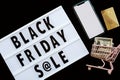 Creative promotion composition Black friday sale text on lightbox on black background, next grocery trolley, mobile phone, credit Royalty Free Stock Photo