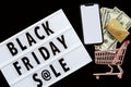 Creative promotion composition Black friday sale text on lightbox on black background, next grocery trolley, mobile phone, credit Royalty Free Stock Photo