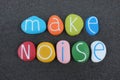 Make Noise, motivational slogan composed with multicolored stone letters over black volcanic sand Royalty Free Stock Photo