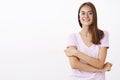 Creative and smart good-looking female student in roung glasses and blouse holding hand on arm in shy insecure posture Royalty Free Stock Photo