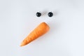 Creative snowman face made of carrots and black Christmas balls on a white background.