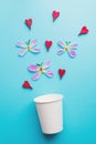 Paper coffee cup, butterflies made of fresh flower petals and red wooden hearts isolated on pastel blue background Royalty Free Stock Photo