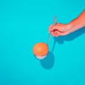 A creative summer composition with a hand holding a grapefruit in a ladle. Minimal fruit concept on a blue background.