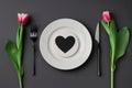Creative table setting with hearts on a white plate black fork and knife tulips on a dark background.
