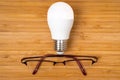 Creative thinking concept with glowing light bulb and glasses on wooden background Royalty Free Stock Photo