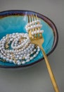 A creative vertical frame with a turquoise plate, a gold fork, and pearl necklaces imitating spaghetti