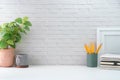 Creative workspace with blank poster frame, coffee cup, books and flower pot on white table with brick wall Royalty Free Stock Photo