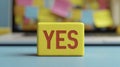 Creative workspace featuring a colorful yes block on a blue table with a blurred background of sticky notes Royalty Free Stock Photo