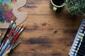 Creative workspace with paint brushes, watercolors and palette on wooden desk.