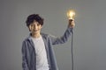 Boy holding glowing light bulb lamp standing isolated on grey studio copy space