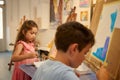 Adorable talented kids, little artists standing in front of easel, holding brush and palette, drawing in fine art studio