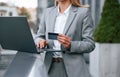 Credit card payment. With laptop. Woman in formal clothes is outdoors near the business building