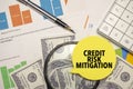 CREDIT RISK MITIGATION words on yellow sticker with dollars with calculator and pen