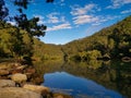 Beautiful view of creek with reflections blue sky, light clouds, fog, mountains and trees on water Royalty Free Stock Photo