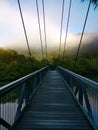 Beautiful view of creek with reflections suspension bridge, blue sky, light clouds, fog, mountains and trees on water Royalty Free Stock Photo