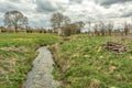 Creek surrounded by fields covered in greens under the cloudy sky in England