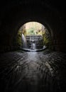 Creepy dark eerie old sewer brick tunnel spooky shadows water river running through flowing light at the end. Waterfalls long.