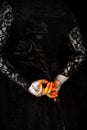 Creepy halloween vampire hands close up in red orange and silver holding black rose