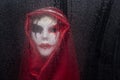 Creepy horror mask with cloak with raindrops on window glass