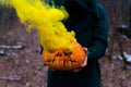 A creepy witch holds a steaming pumpkin in a deep forest. Jack o lantern emits yellow smoke for halloween Royalty Free Stock Photo