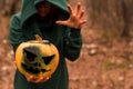 A creepy witch holds a steaming pumpkin in a deep forest. Jack o lantern emits yellow smoke for halloween Royalty Free Stock Photo