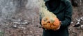 A creepy witch holds a steaming pumpkin in a deep forest. Jack o lantern emits yellow smoke for halloween Royalty Free Stock Photo