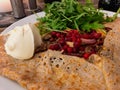 A crepe or galette filled with fried meat, mushrooms, lingonberry, rocket sallad and creme fraiche