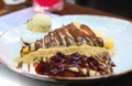 Crepes with chocolate cream. Pancakes with chocolate paste, hazelnuts, cherry sauce and a scoop of ice cream on a white plate on a Royalty Free Stock Photo