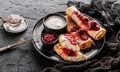 Crepes with cottage cheese, fruit jam, cherries, sour cream and icing sugar on black plate over dark background