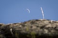 A crescent moon rises behind rocks