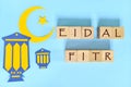 Crescent moon, star and lantern decoration with text on wooden blocks flat lay in blue background. Eid al fitr celebration Royalty Free Stock Photo