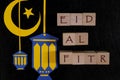 Crescent moon, star and lantern decoration with text on wooden blocks flat lay in dark black background. Eid al fitr celebration Royalty Free Stock Photo