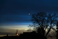 Crescent moon and a star in a quiet nighttime scene with silhouetted house and tree against a dark blue sky during