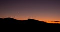 Crescent moon and sunset over silhouette of desert ridge on fall evening Royalty Free Stock Photo