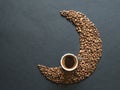 Crescent shape made of coffee beans and a cup of black coffee on black background. Top view