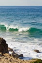 Cresting breaking wave on shoreline edge with washback foam on sandy shoreline with boulders