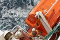 Crew member with orange jacket and helmet checking aft hook on life boat fixed to container vessel, second seaman in white overall Royalty Free Stock Photo