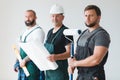 Three professional builder with painting roll and renovation plans standing in empty interior