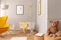 Crib with a yellow blanket, armchair, teddy bear in a toddler room interior. Real photo