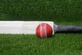 Cricket bat and red ball on green grass background Royalty Free Stock Photo