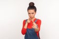 Crime, killing gesture. Portrait of dangerous girl with hair bun in denim overalls imitating guns, shooting into camera