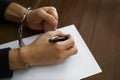 Criminal in handcuffs writing confession at desk