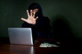 Criminal man in black hood with laptop computer, a gun and money at the at desk reaching out his hand to camera , mask thief Royalty Free Stock Photo